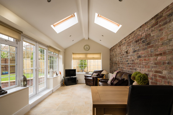 brick wall accent in living room conservatory with brown leather sofas television and skylight windows